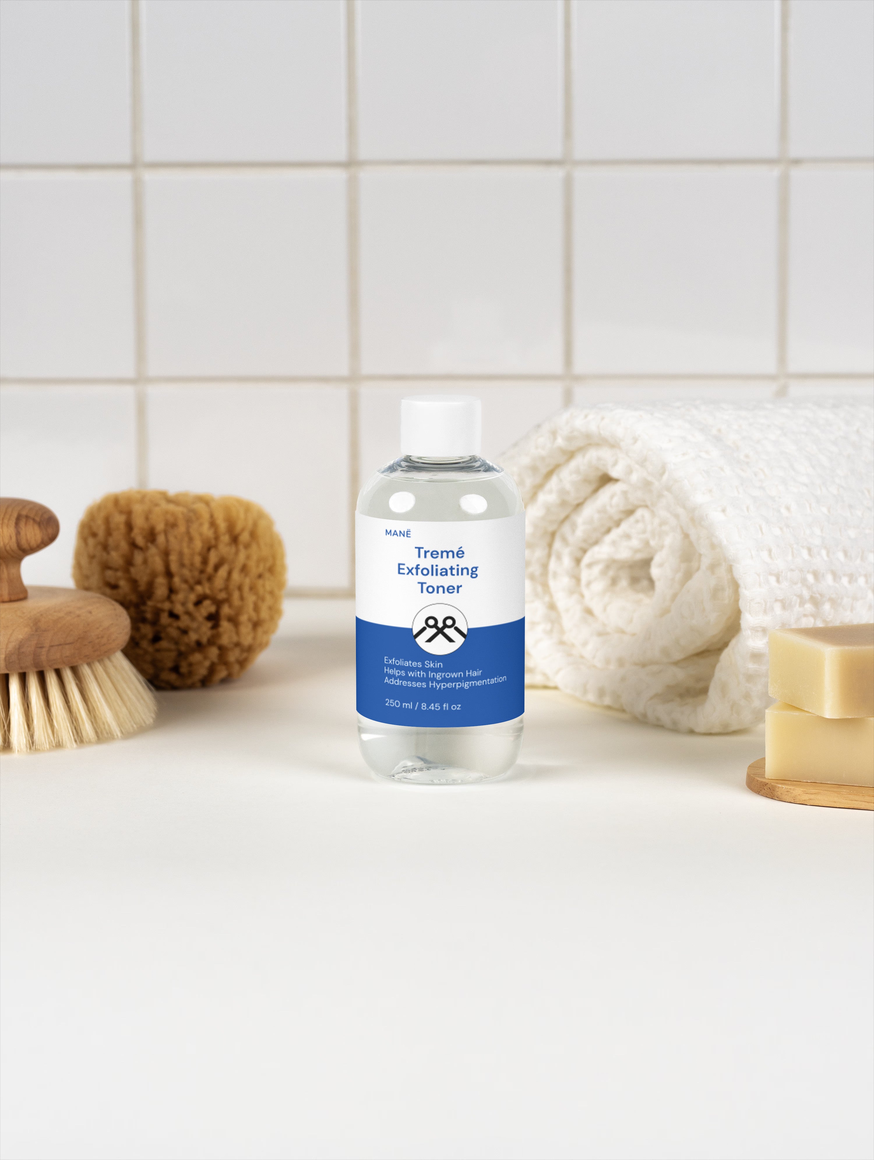 MANË Tremé Exfoliating Toner in its clear bottle with white cap, beside towels